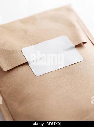 Mockup of a brown kraft paper envelope with a blank white rectangular sticker, close-up perspective view. Stock Photo