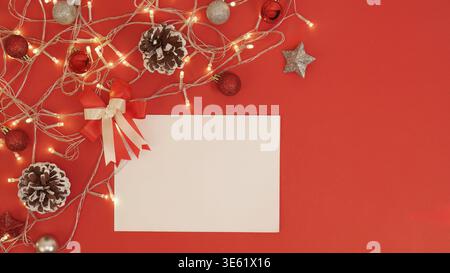 A blank card surrounded by Christmas decorations, pine cones, and lights on a red background, ideal for holiday messages Stock Photo