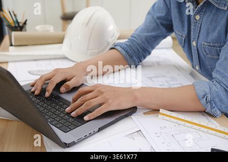Close-up of an architect and engineer using a laptop while reviewing blueprints. A professional workspace for project planning Stock Photo
