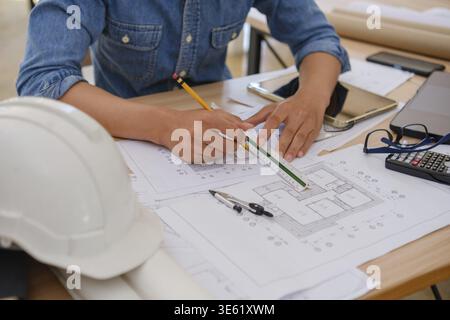 Close-up of an architect and engineer using a pencil and ruler to draft blueprints. The desk is filled with essential tools, including a calculator, c Stock Photo