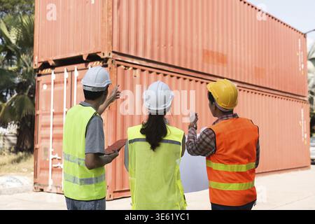 Three construction professionals, including two male workers and a female supervisor, strategize and discuss project logistics while observing shippin Stock Photo