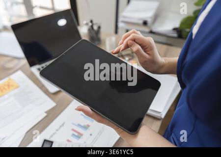 An accountant examines financial data on a tablet, surrounded by tax documents, reflecting modern technology in finance Stock Photo