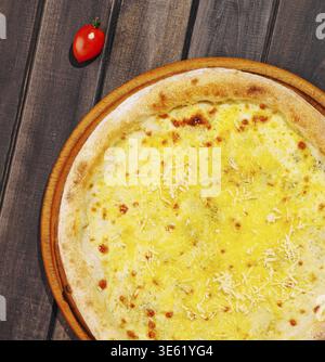 Food, Mouthwatering cheese pizza on a round wooden plate placed on a rustic wooden table. A vibrant cherry tomato adds a pop of color nearby, enhancin Stock Photo