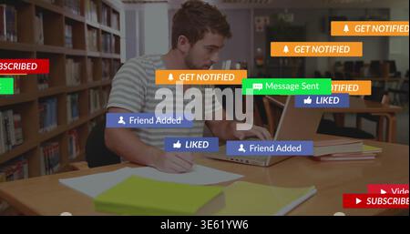 Studying male student writing notes with pen while using laptop at library, striped tee, overlays Stock Photo