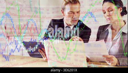 Analyzing man in suit and woman in blazer scanning documents at meeting table, with laptop charts Stock Photo