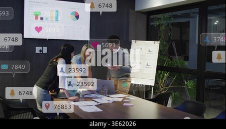 Reviewing three staff in business attire examining printed charts and laptop at conference table Stock Photo