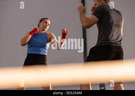 Male and female sparring in ring with ropes, woman wearing blue top and red hand wraps Stock Photo