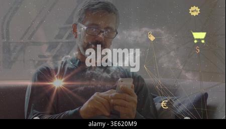 Tapping senior man in dark top and glasses on sofa using smartphone with digital commerce overlays Stock Photo