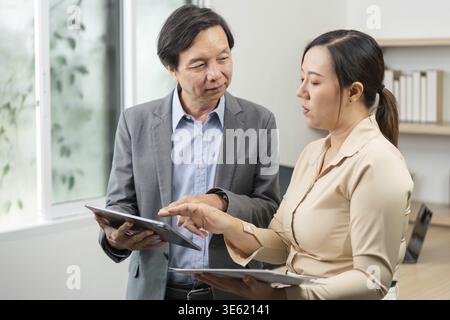 A man and woman engage in a focused discussion while reviewing data on tablets, highlighting teamwork and professional interaction Stock Photo