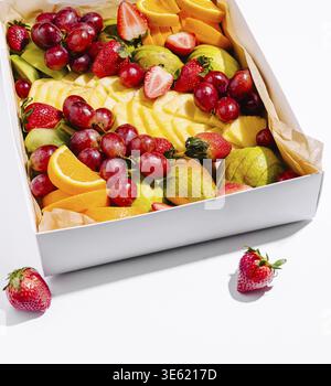 Food, A vibrant box filled with assorted fresh fruits, including strawberries, grapes, oranges, and apples, perfectly arranged on a clean white backgr Stock Photo