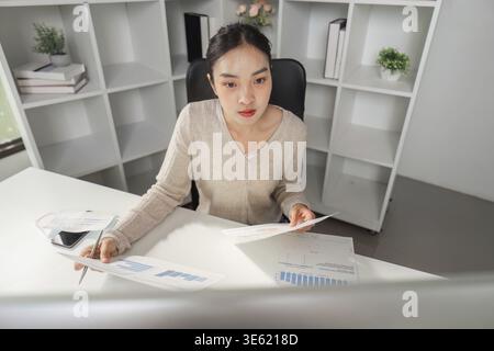 A professional office worker examines financial documents and charts, highlighting focus and analytical skills in a modern office environment Stock Photo