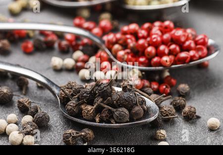 Colorful peppers in spoon on black table - cubeb, pink, green and white closeup. Spices. Selective focus Stock Photo