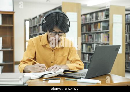Thoughtful Young Student Preparing for Class, Doing Homework on a Laptop Computer. Freelance Journalist Working on an Article in a University Library Stock Photo