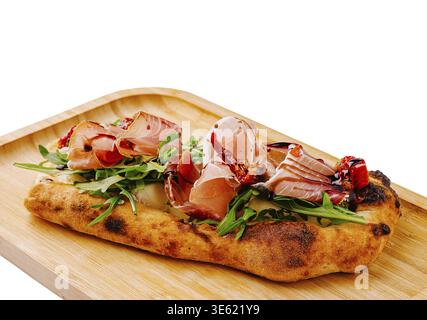 Food, A freshly baked focaccia bread is topped with arugula, sliced ham, and roasted red peppers. The dish is elegantly presented on a wooden serving Stock Photo