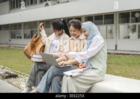 A diverse group of female students engaging in collaborative work on a laptop outside on a university campus, showcasing friendship and academic enthu Stock Photo