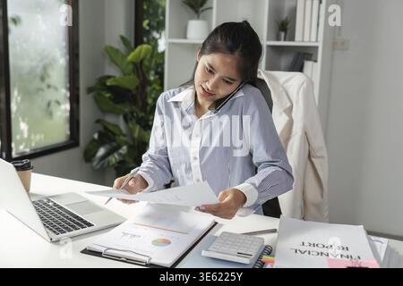 An accountant engages in a phone call while organizing financial reports and calculations, showcasing multitasking in a professional setting Stock Photo