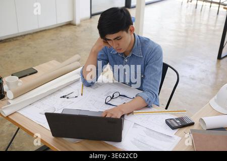 A focused architect and engineer using a laptop to work on blueprints. Concentrated on design and planning, they are engaged in creating precise and d Stock Photo