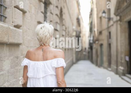 A woman in a white dress walks down a narrow street. Concept of solitude and quietness, as the woman is the only person visible in the scene. The stre Stock Photo
