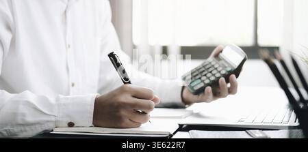 Close up Business man using calculator and laptop for do math finance on wooden desk in office and business working background, tax, accounting, stati Stock Photo
