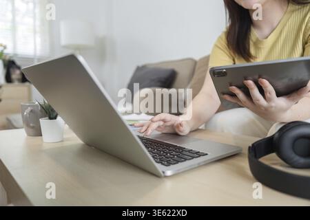 A dedicated professional works diligently at her home office, effectively multitasking between her laptop and tablet in a comfortable environment Stock Photo