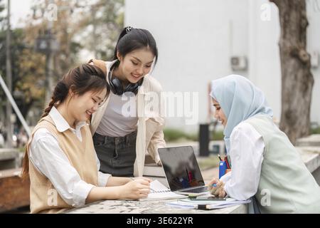 A diverse group of female students collaborating on studies with a laptop and notepad at an outdoor workspace, demonstrating teamwork and engagement i Stock Photo