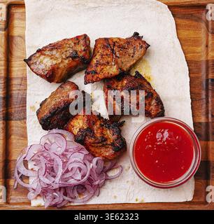Food, Tender grilled meat pieces are beautifully arranged on a flatbread, accompanied by sliced onions and a small dish of spicy sauce, creating a mou Stock Photo