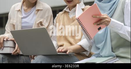 Close-up view of diverse students engaging in study with a laptop and notebooks while sitting outdoors at a university campus Stock Photo