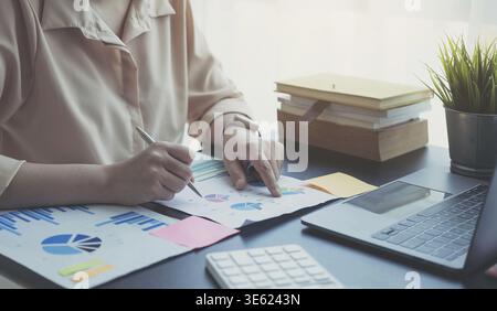 Woman checking paperwork from accounting department to analyse number on document, using laptop check business database, information comparing. Typing Stock Photo