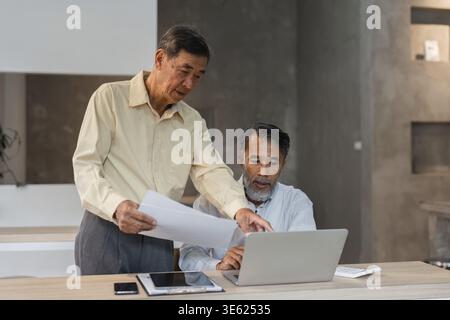 In a collaborative environment, two experienced professionals assess data on a laptop, highlighting teamwork and strategic processes in business Stock Photo