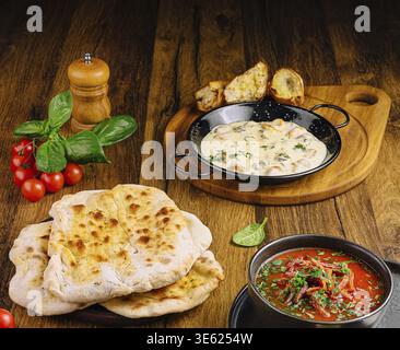 Food, A tempting spread featuring naan bread, a creamy curry dish, and fresh tomatoes and basil on a rustic wooden table. The meal highlights vibrant Stock Photo