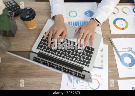 A business professional engaged in remote work, analyzing financial graphs and reports on a laptop, showcasing productivity and focus Stock Photo