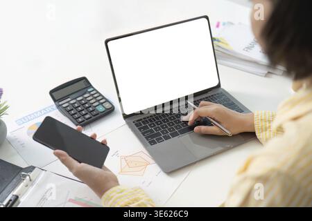 A focused woman working remotely, using a laptop and calculator to analyze financial reports and data Stock Photo