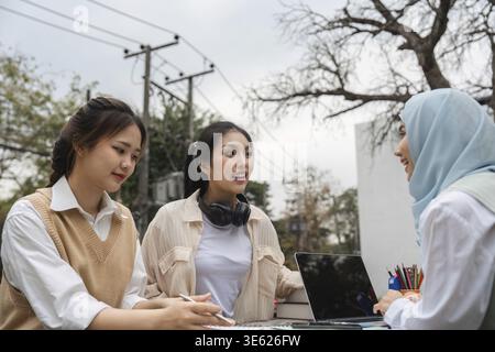 A diverse group of university students engaged in a serious discussion outdoors, collaborating on academic projects with a laptop and notebooks Stock Photo