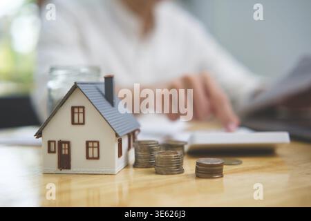 Real estate investment and mortgage calculation concept with businessman using calculator, coins stacked on desk, laptop, and small house model, repre Stock Photo