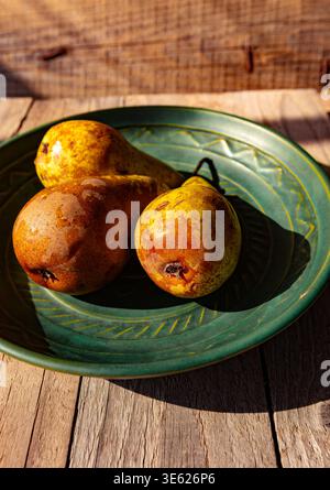 Rustic still life of three ripe Bosc pears on a green ceramic plate over a weathered wooden surface in natural sunlight Stock Photo