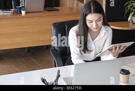 Young asian businesswoman works on tablet with laptop at the office Stock Photo