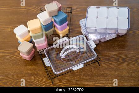 Colorful meal prep boxes and a clear plastic case containing small white containers rest on metal cooling grids. Stock Photo