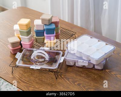 Pastel kitchen storage items and clear cases holding small white containers lie on dark grids. A wide-angle horizontal shot captures the silicone molds. Stock Photo