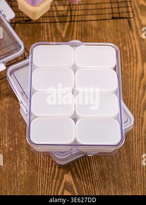 A transparent plastic case holds eight small white square food storage containers in a neat 2-by-4 grid. Stock Photo