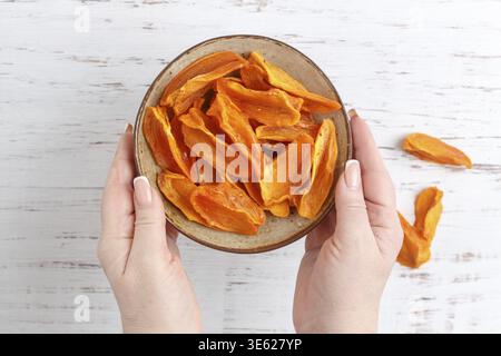A woman holds a plate with slices of ripe dried persimmon in a plate on the table. A healthy snack. A treat. Selective focus, top view Stock Photo