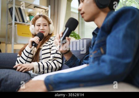 Young man and woman having podcast conversation at home using microphones and headphones while sitting on sofa Stock Photo