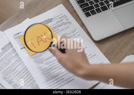 A hand holds a magnifying glass over tax documents, emphasizing attention to detail in financial matters Stock Photo