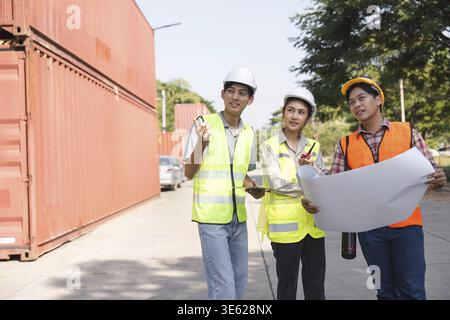 A diverse construction team, comprising an engineer, a project manager, and a worker, discussing project blueprints and plans at a bustling constructi Stock Photo