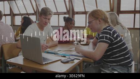 Working students in shirts and hoodie collaborating at school desks, with laptop and calculator Stock Photo