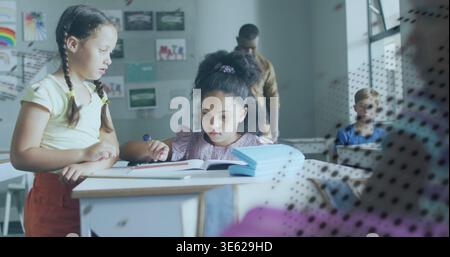 Reading student in mauve top focusing on open book at school while classmate pointing at pages Stock Photo