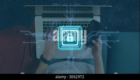 Typing woman in striped top with wristband, using laptop, holding phone on sofa, showing lock icon Stock Photo