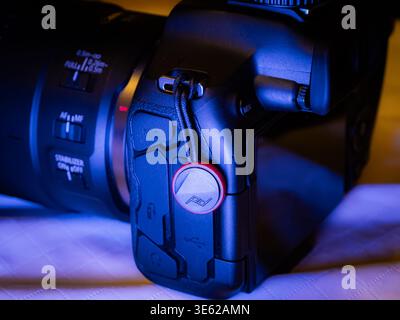 Canon EOS R series mirrorless camera showing side ports, lens details and a Peak Design anchor link under blue lighting Stock Photo