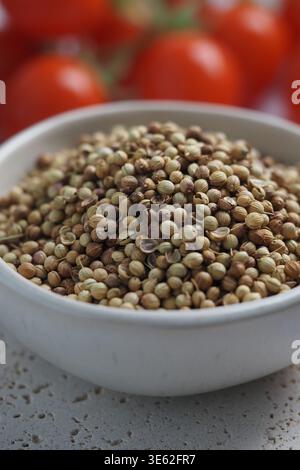 Coriander seeds placed in a bowl with tomatoes in background Stock Photo
