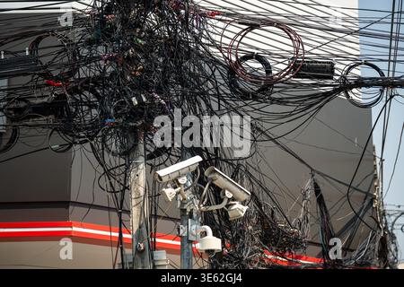 Messy tangled electricity wires and data cables on pole, asian urban landmark at street in city. Stock Photo