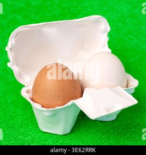 Brown and white fresh eggs inside cardboard paper package on green  fake grass background macro Stock Photo